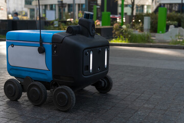 Close-up view of blank blue and white autonomous food delivery robot driving on city street. Soft focus. Copy space for your text or decoration. Urban technology theme.