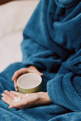 Person wrapped in blue blanket holding cup of water and tea