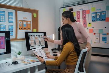 Two women ux ui designers working together discussing mobile app interface wireframe design on computer screen at modern office