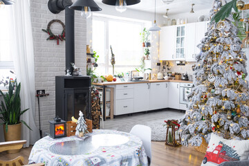 Festive white modern interior of house is decorated for Christmas and New Year in loft style with black stove, fireplace, Christmas tree. Potted plants, firewood in the woodpile