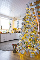 Festive Christmas decor in white kitchen, modern village interior with a snowy Christmas tree and fairy lights. New Year, Christmas mood, cozy home, Metal modular staircase. The general plan