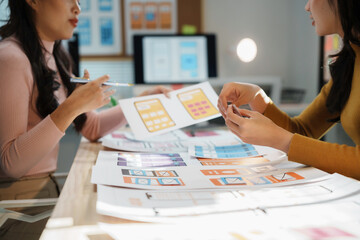 Two female uiux designers are discussing the user interface design of a mobile application,...