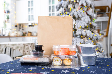 Delivery of sushi and rolls in food containers on the table in the festive interior of the kitchen of the house with a white Christmas tree for Christmas and New year. Food delivery for the holidays