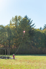 Young caucasian girl playing with a pink balloon on a long string in a park in autumn