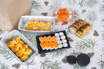 Delivery of sushi and rolls set top view on the table with a Christmas decor with a Christmas tree and a tablecloth with snowflakes, home cooking