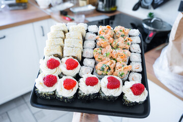 Delivery of sushi and rolls set is hold in hand in the interior modern kitchen of house 