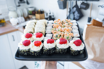 Delivery of sushi and rolls set is hold in hand in the interior modern kitchen of house 