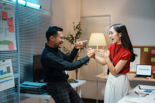 Two business colleagues are playfully pointing at each other and laughing during a late night at the office
