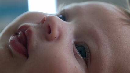 Extreme close-up of a baby’s face, focusing on the eye and nose. baby lies on a bed, gazing upward in a calm and serene manner, details of the baby’s facial features