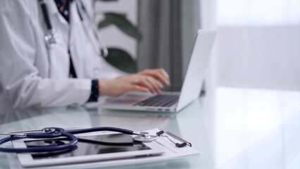 Tablet computer and blue stethoscope are on the glass table while doctor woman is using laptop computer on the glass table. Medicine concept