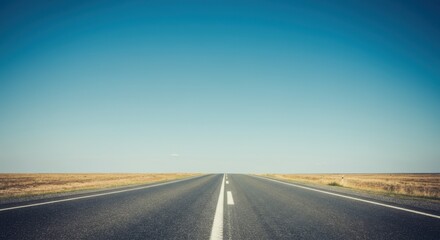 Naklejka premium Straight empty road through barren landscape under clear blue sky
