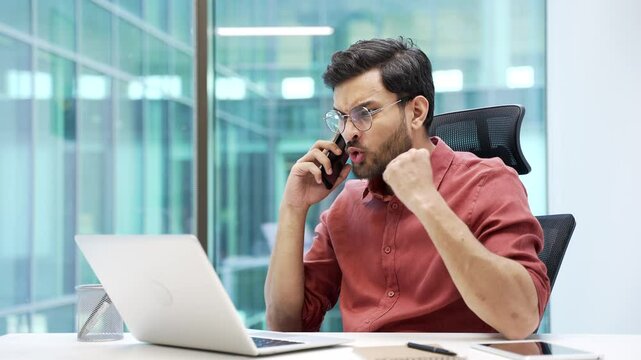 Angry dissatisfied businessman in glasses arguing talking on phone sitting at workplace in business office. Excited executive emotionally talks with subordinate about problems that need to be solved