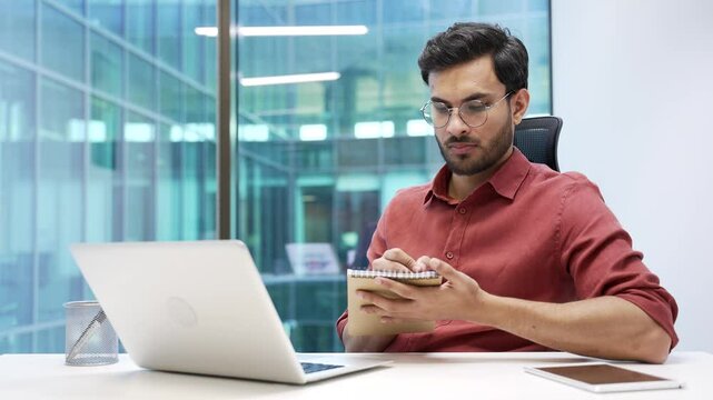 Businessman watching video call online conference notes in notebook looking at laptop computer screen sitting at workplace in office. Adult man worker on remote business meeting, seminar or training