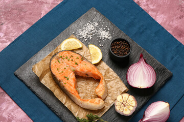 Slate board of tasty salmon steak with garlic, onion and lemon on purple background
