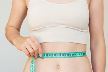 Close up portrait of young Caucasian woman in beige underwear measuring her slim waist...