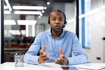 Mature businessman wearing headset in modern office engaged in video call, discussing business...