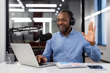 Mature businessman wearing headphones conducting virtual meeting using laptop and microphone....