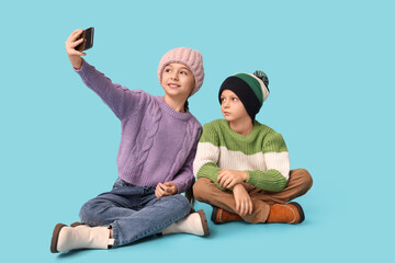 Cute little children in warm winter clothes taking selfie on blue background