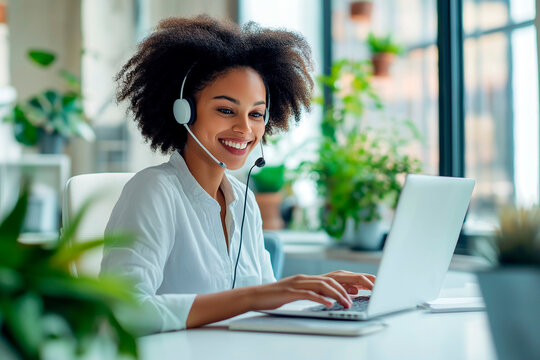Smiling woman with a headset working on a laptop in a bright office with plants