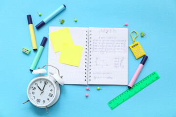 Notebook with alarm clock and school stationery on blue background