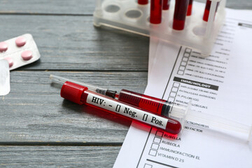 HIV blood test tube, syringe and laboratory report form on grey wooden background