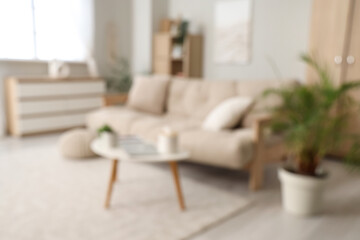 Blurred view of light living room with couch, table and chest of drawers