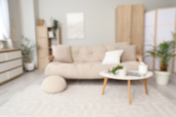 Blurred view of light living room with couch, table and folding screen