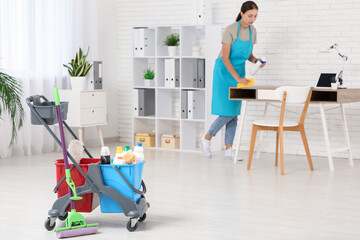 Female janitor with trolley and cleaning supplies cleaning office