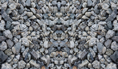 Close-up of a textured rock pattern with gray and white stones. A symmetrical arrangement of rough stones creating a natural mosaic. Natural stone texture with a unique mirrored pattern.