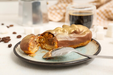 Plate with sweet eclair and coffee on light  background