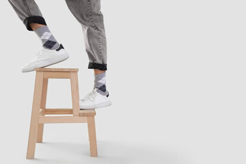 Young man in sneakers on step stool against light background