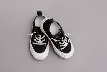 Child's black sneakers on the grey background. Fashion kids outfit. Flat lay, top view. Set of kids clothes and accessories for spring or autumn.