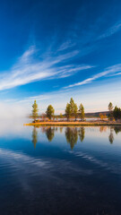 Fototapeta premium Calm water reflects trees during autumn morning in the Lapland arctic nature during ruska session with blue sky and sunshine evokes calm, peaceful and solitude, Finland