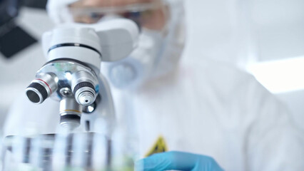 Professional scientist in protective gear is using microscope in a laboratory setting, close-up. Science and medicine concepts