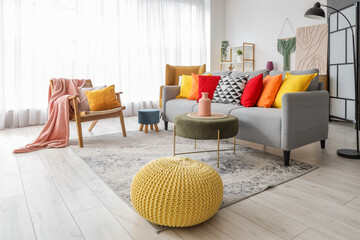 Interior of stylish living room with colorful cushions on sofa, armchair and poufs