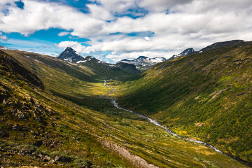 Scenic breathtaking pview of nordic nature with snow covered mountains and deep valley with running stream in the heart of Jotunheimen national park in Norway during beautiful summer day when hiking