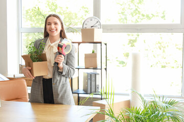 Young businesswoman with cardboard box and adhesive tape in office on moving day