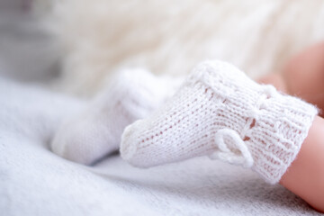 Newborn baby feet wearing soft knitted white booties on a cozy blanket in a warm indoor setting