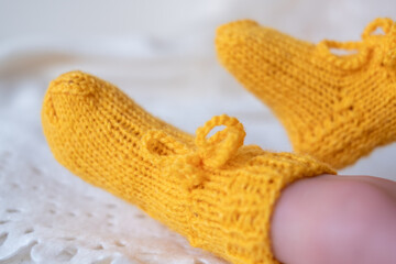 Bright yellow hand knitted baby booties adorning a small childs feet on a soft white textured background