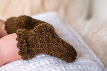 Cozy knitted baby booties in warm brown resting on a soft white blanket indoors during the afternoon light