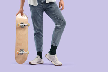 Young man in sneakers with skateboard on lilac background