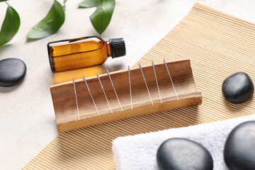 Acupuncture needles, oil, towel and spa stones on light background