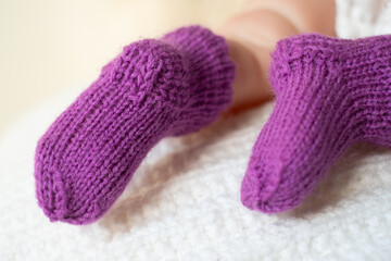 Cozy purple knitted socks on a baby\'s feet resting comfortably on a white blanket indoors