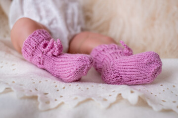 Adorable baby feet in pink knitted booties resting on soft fabric during a cozy indoor moment