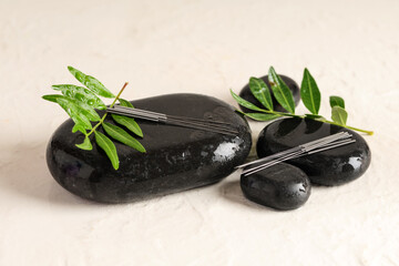 Acupuncture needles and spa stones on light background