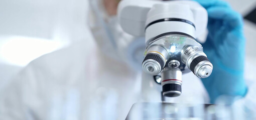 Professional scientist in protective gear is using microscope in a laboratory setting, close-up. Science and medicine concepts