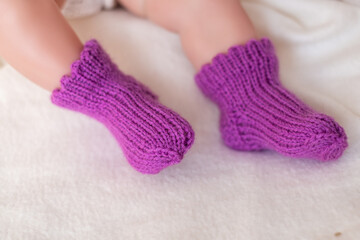 Adorable baby feet wearing hand-knit purple socks on soft cream fabric during a cozy afternoon at home