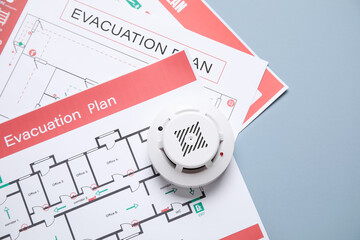 Modern smoke detector with evacuation plans on grey background