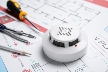 Modern smoke detector with supplies on evacuation plans, closeup