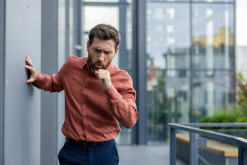Businessman coughs in outdoor office environment, evoking themes of health, stress, and respiratory...